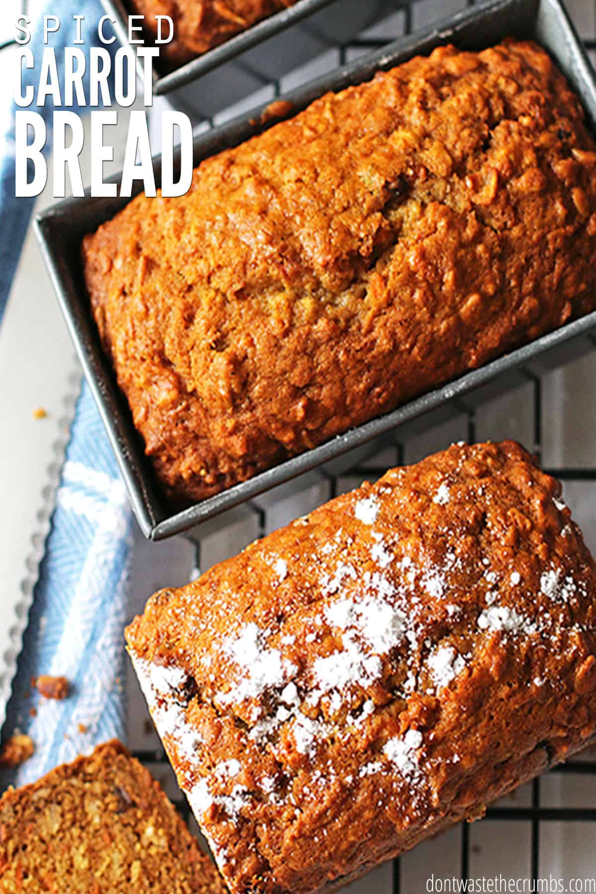 Two carrot bread loaves, one still in the loaf pan and one dusted with powdered sugar, sit atop a blue and white towel. Text overlay reads "Spiced Carrot Bread."