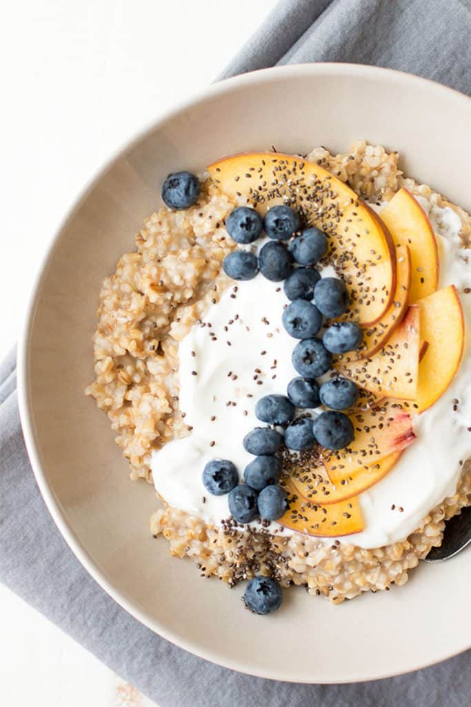 A bowl of steel cut oats is ready to serve with fresh yogurt and fruit toppings.