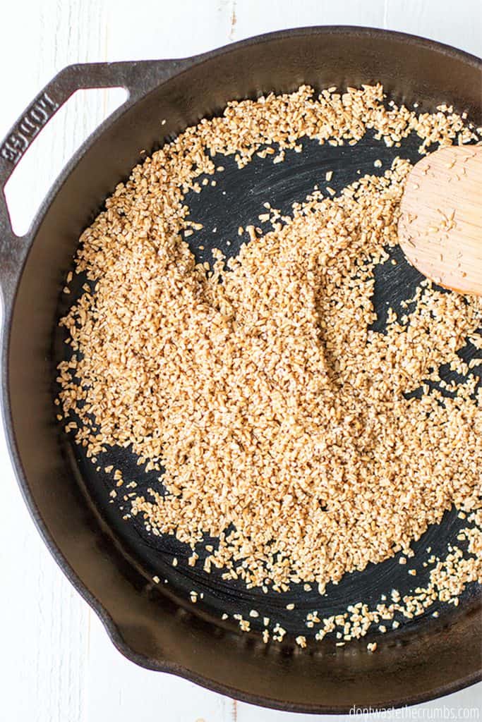 Steel cut oats line the bottom of a cast iron skillet.