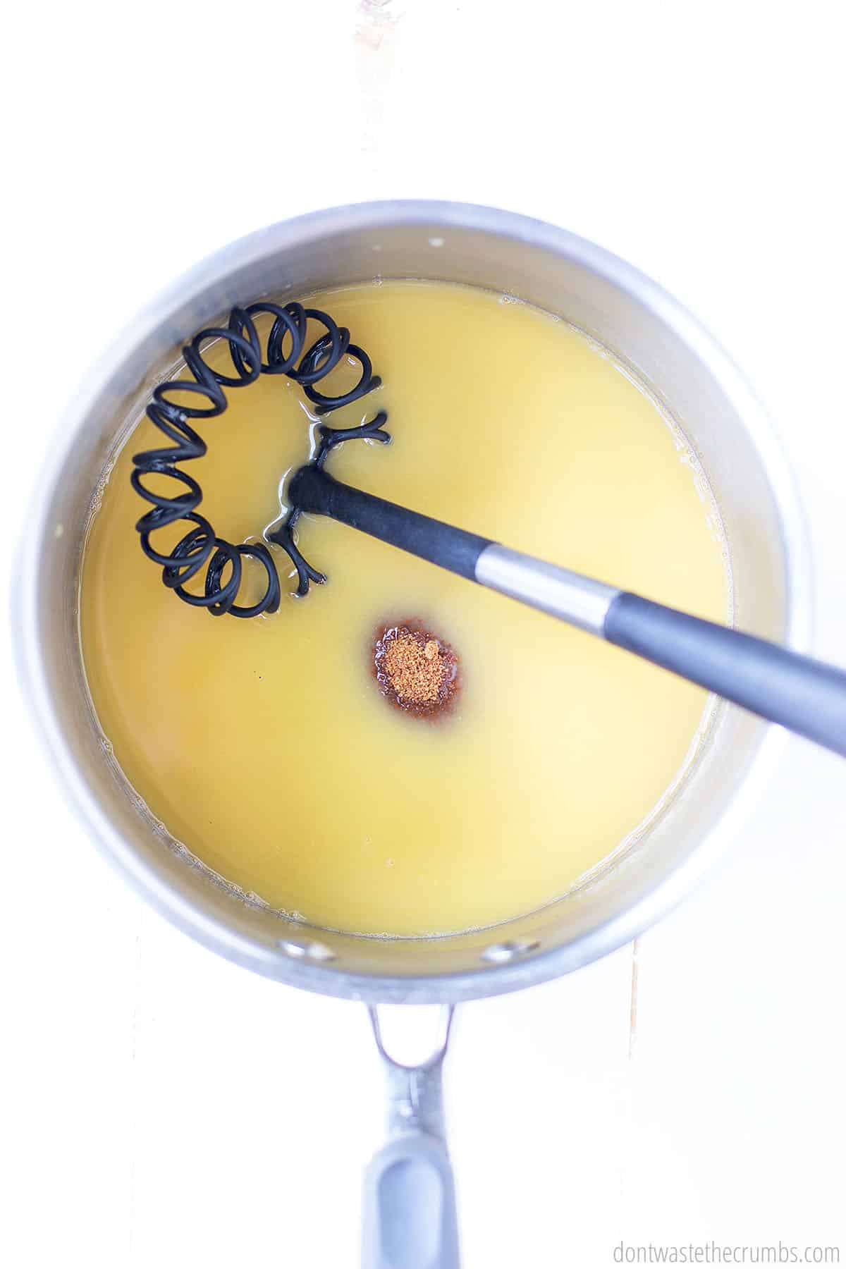 A saucepan with a whisk inside ready to mix up the base (pineapple juice, vinegar, soy sauce and brown sugar) of a sweet and sour sauce recipe.