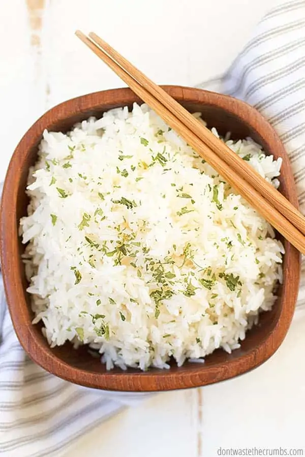 A wooden bowl is filled with white rice and topped with chopped herbs.