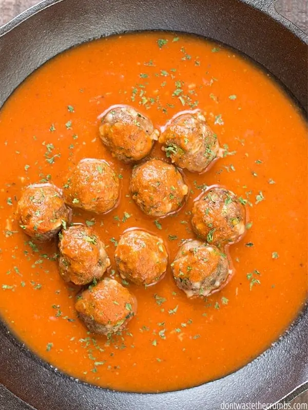 A skillet is filled with rich tomato sauce and meatballs, sprinkled with dried herbs.