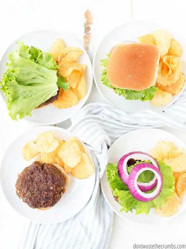Four burgers are served up on homemade buns with a side of potato chips and topped with lettuce and shredded onion.