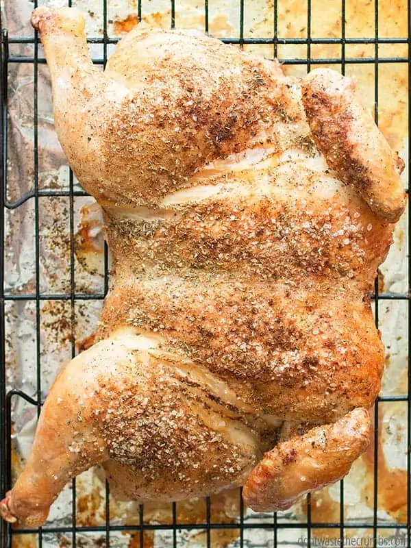 A fully roasted whole chicken rests on a baking rack to cool.