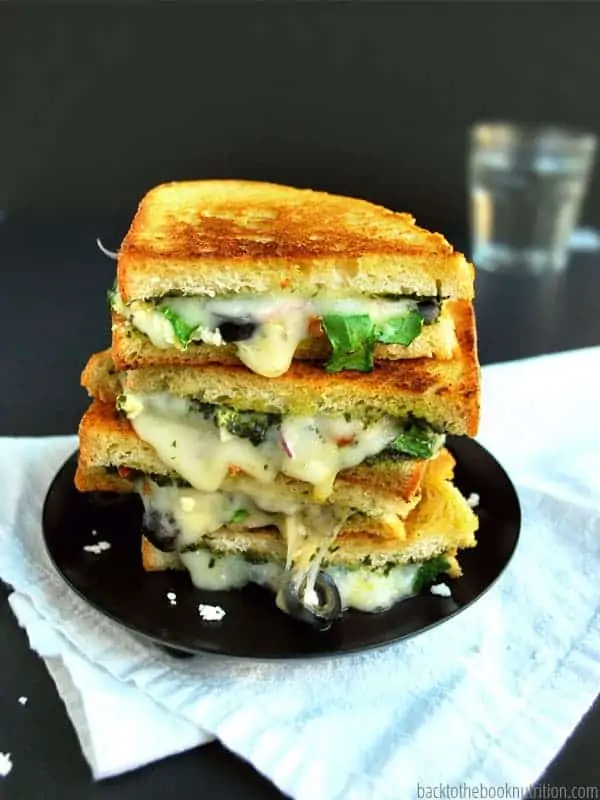 A three-layer grill cheese is melted to perfection and filled with olives, lettuce, and cheese.