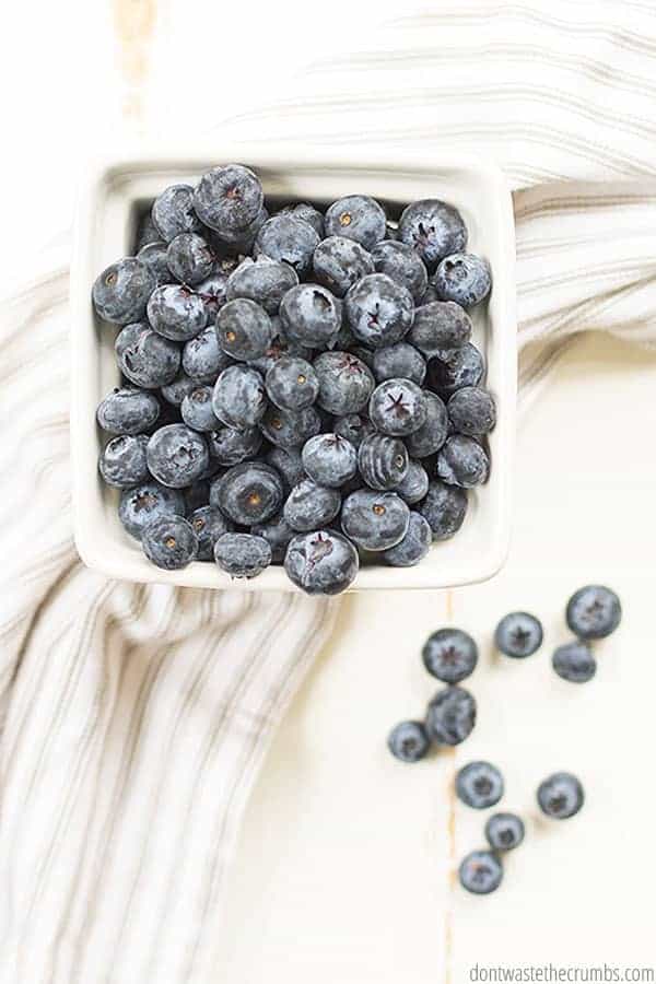 A pint of fresh blueberries overflows onto a towel.
