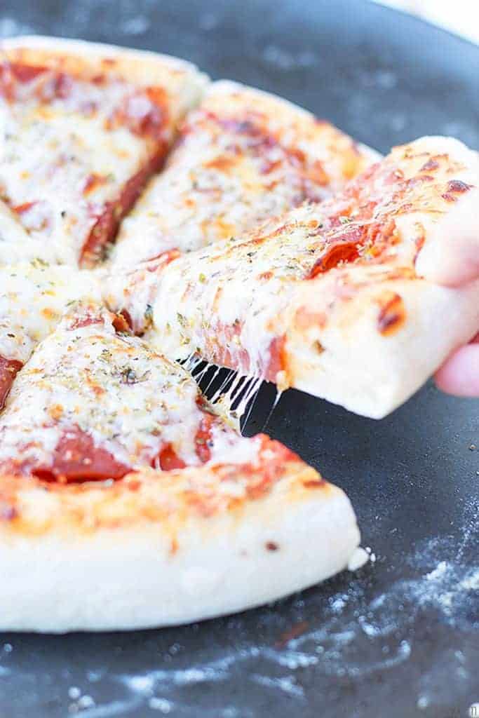 A slice of pizza with gooey mozzerella and pepperoni is pulled from the pan.