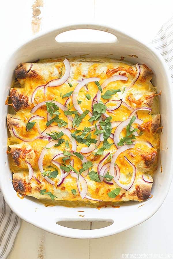 A pan of crispy enchiladas is topped with cheese and slices of red onion and cilantro.