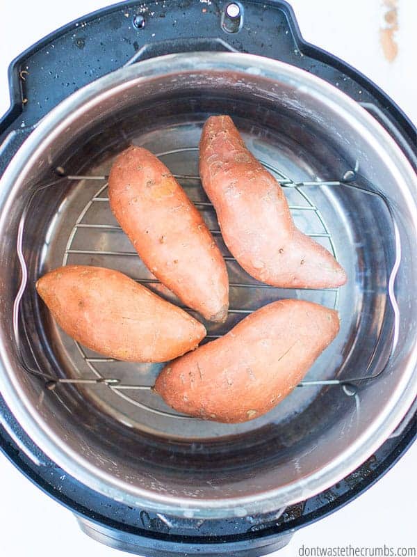 Four uncooked sweet potatoes sit in the trivet of an Instant Pot.