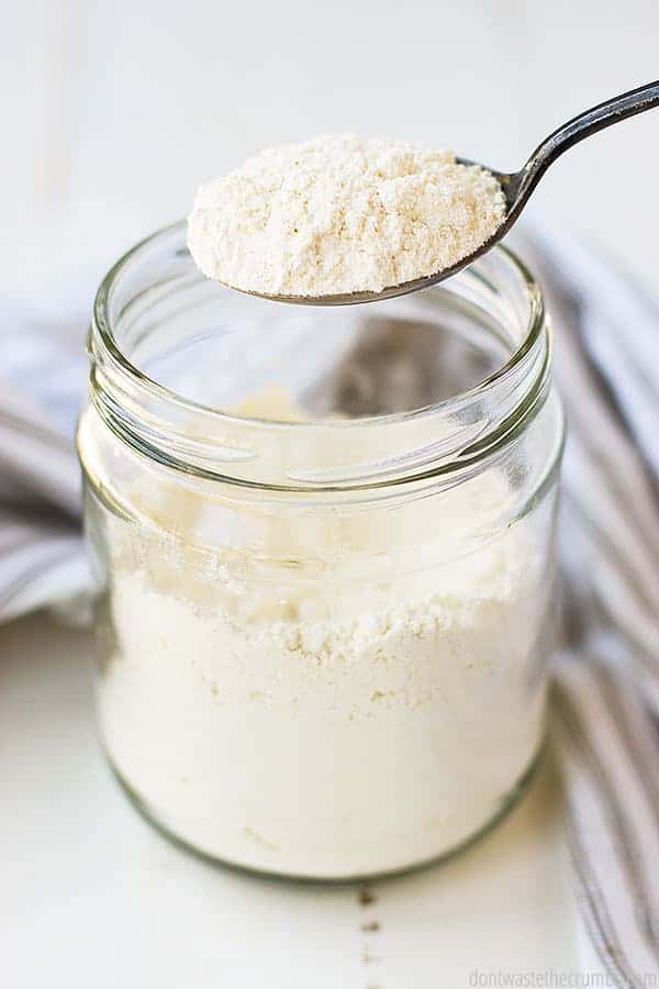 A spoonful of flour hovers over a glass jar filled with flour.