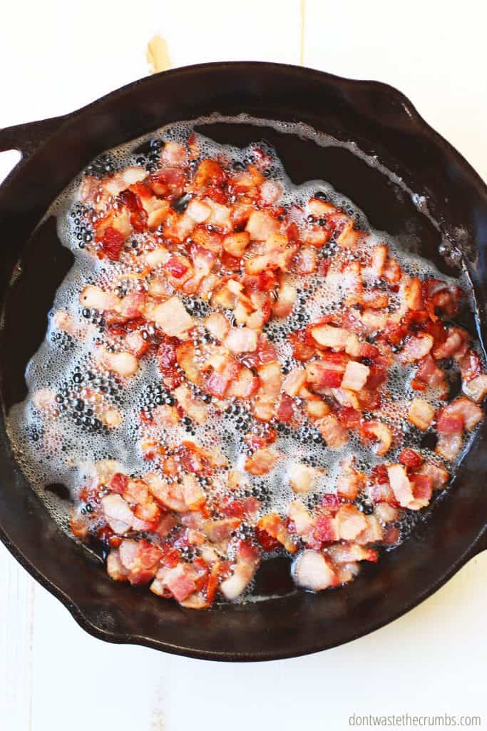 Sliced bacon being cooked in a cast iron skillet, before the Brussels Sprouts and onions are added to the recipe for bacon Brussels sprouts. 