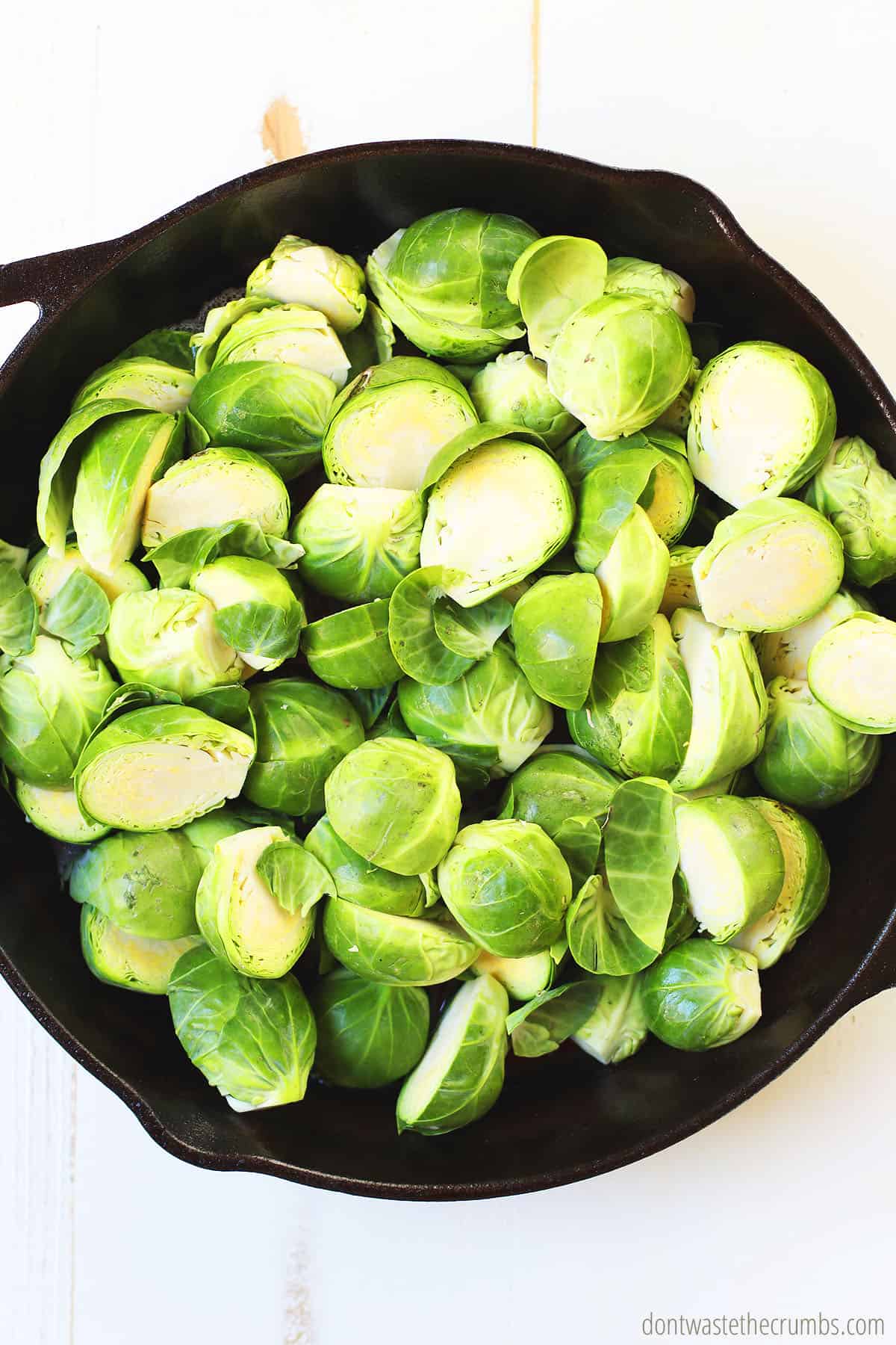 Freshly washed and sliced raw Brussels Sprouts are placed into a cast iron skillet.