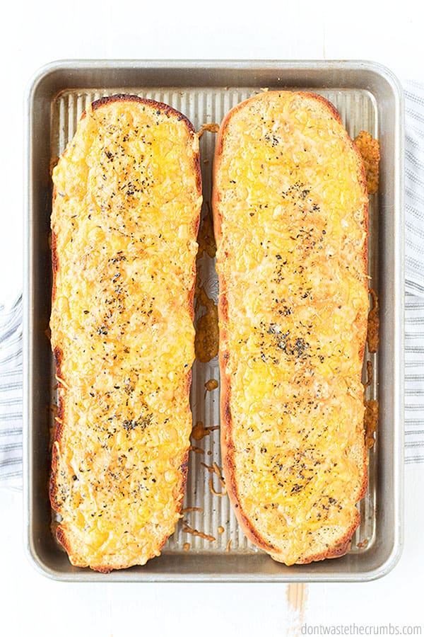 Golden brown Garlic Cheese Bread is hot out of the oven with melty and crispy cheese. It's finished with dried basil and oregano, and ready to be sliced and served. YUM! 