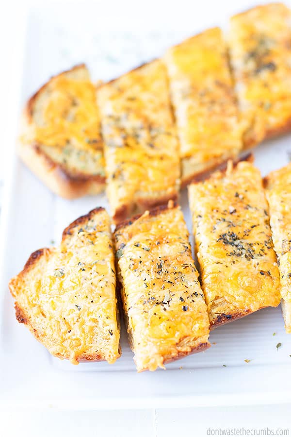 Two half loaves of French bread freshly baked into cheesy garlic bread. Sliced for serving and topped with fresh oregano. 