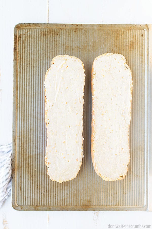 A loaf of French bread sliced in half and with garlic butter smeared all over the sliced surface. 