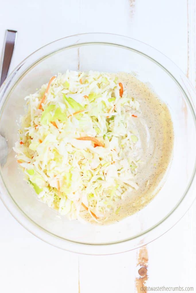 Homemade coleslaw with dressing, shredded cabbage, and shredded carrots before it is mixed up in a clear mixing bowl.