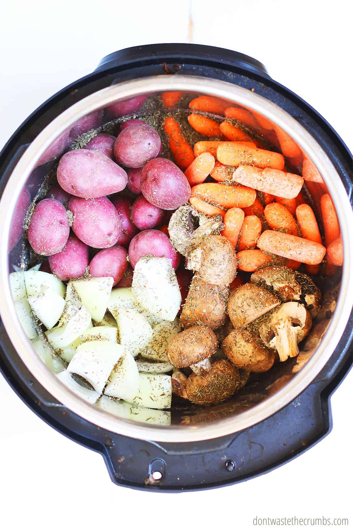 You can use a variety of vegetables. Pictured is a top view of potatoes, carrots, onion, mushrooms, beef, and spices in an Instant Pot.