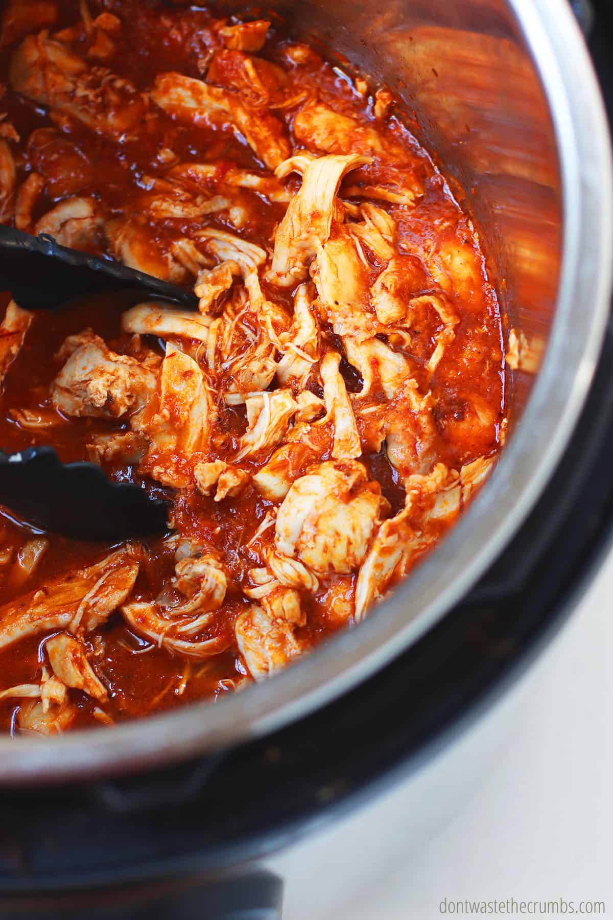 Chicken tinga is finished cooking in the Instant Pot and ready to be served with tongs.
