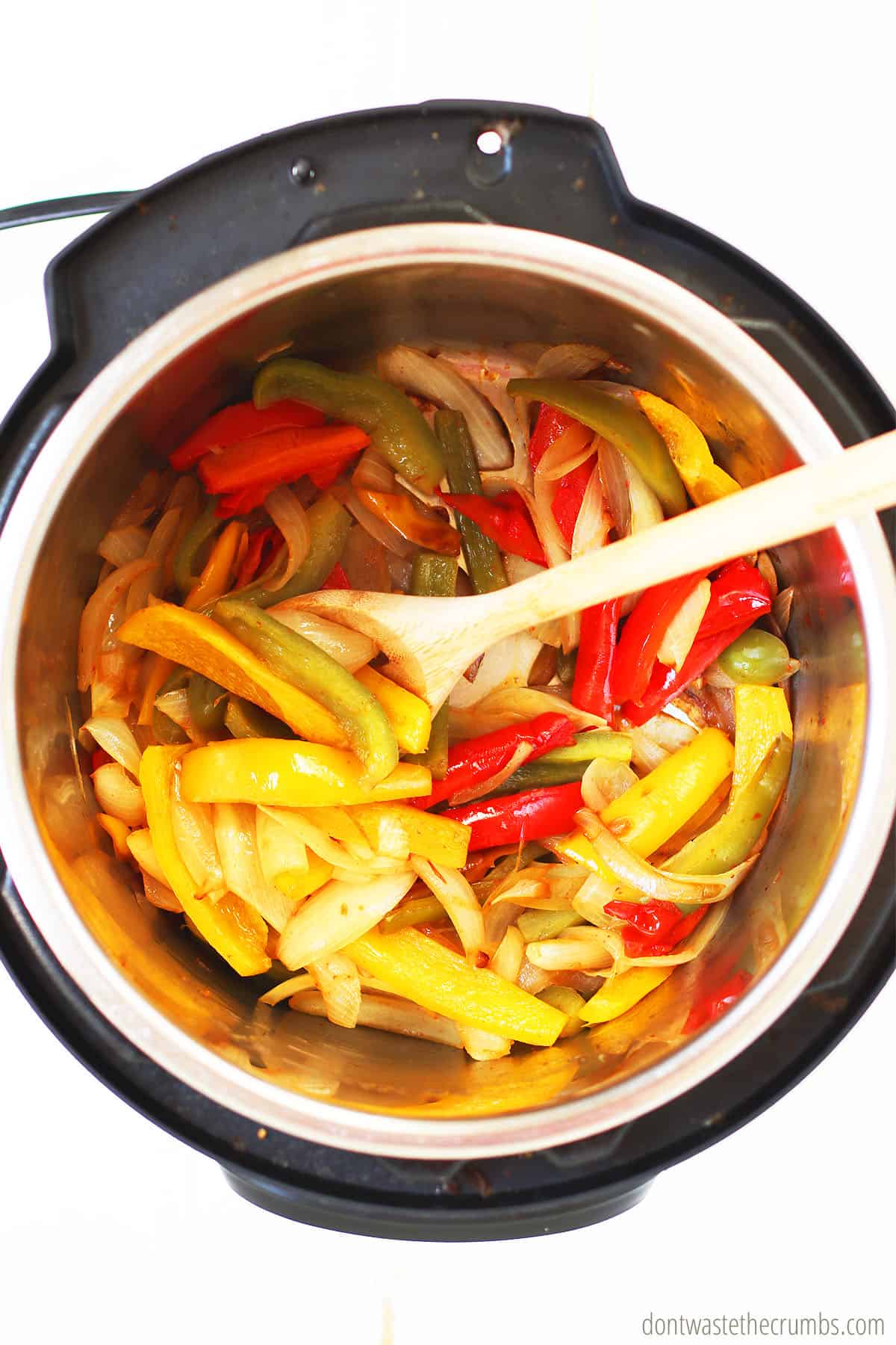 A wooden spoon stirs freshly cooked sliced bell peppers and onions in olive oil and spices. Ready to be served as fajita vegetables.