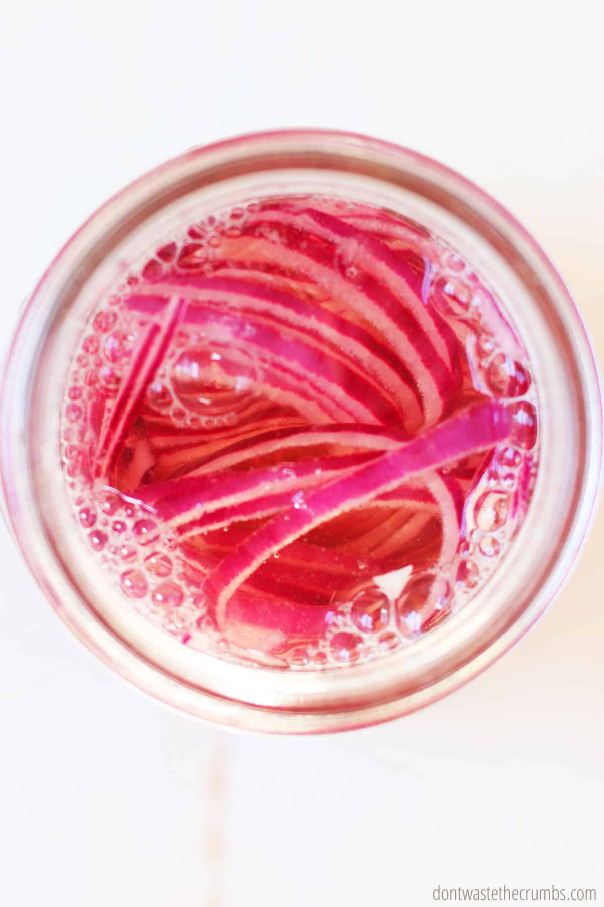 The vinegar has been poured into the glass pint size mason jar with red onions. This is part of the process in making this easy and delicious pickled red onion recipe.