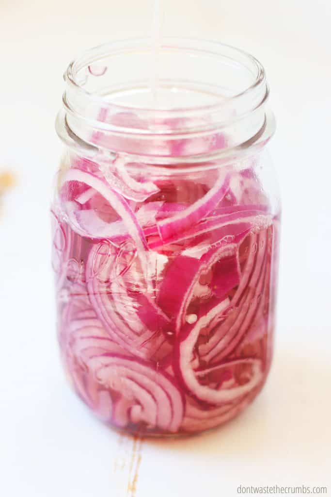 Pictured is a glass pint size mason jar containing raw red sliced onions.