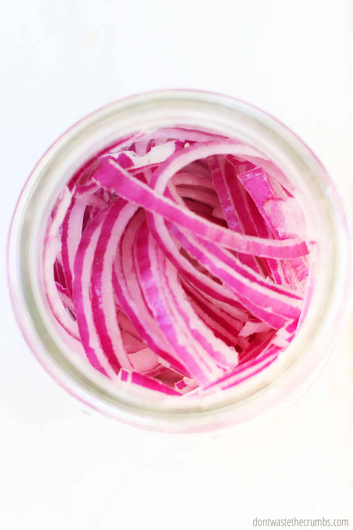 Freshly sliced red onions in a clear glass jar ready to be picked.
