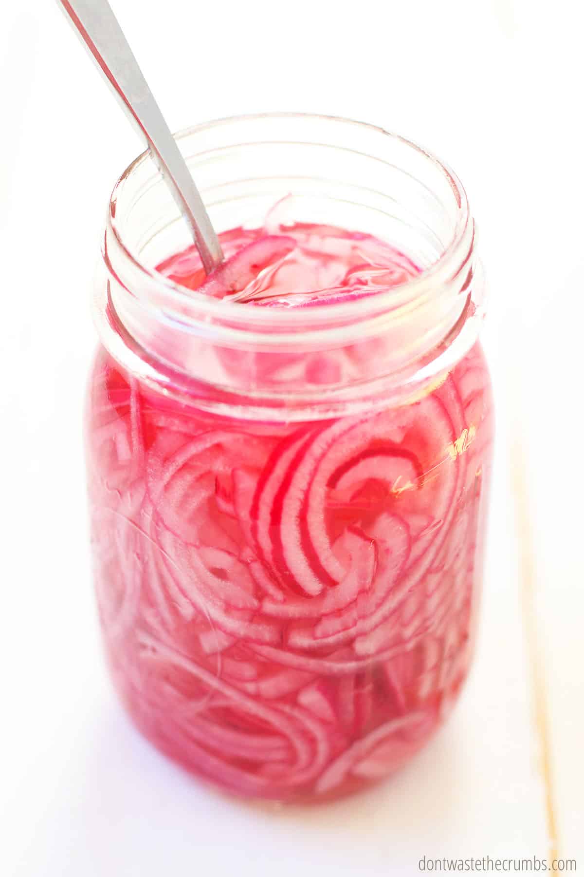 This easy pickled red onion recipe is ready and in a pint size glass mason jar with a spoon inside ready to be scooped.