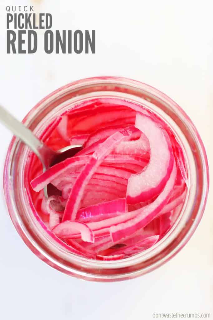 This pickled red onion recipe is easy and quick to make! It's frugal and it goes great with many dishes such as my best burger recipe and Instant Pot beef brisket. Don't forget about breakfast, this serves as a tasty topping for scrambled eggs! You will also learn tips and how to customize this delicious side dish. Pictured is a top view of a mason jar with pickled red onions and a spoon stirring.
