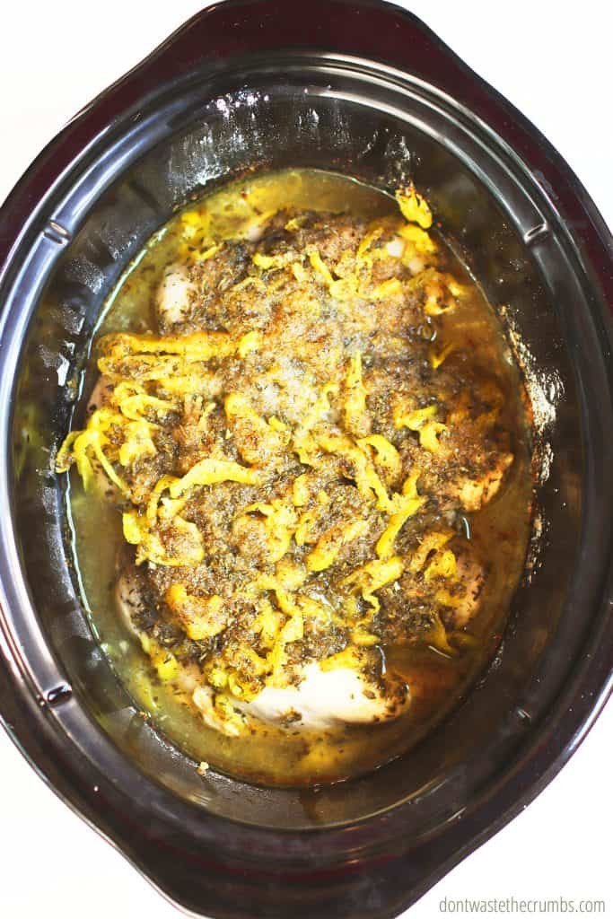 Hot and ready-to-serve Slow Cooker Mississippi Chicken in an oval Crock Pot. The freshly roasted pepperoncini looks delicious on top of the browned chicken.
