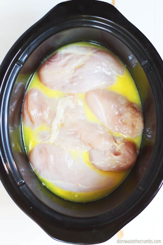 Raw chicken on the bottom of the slow cooker with the cooking liquid poured over, getting ready for the pepperoncini to be added. 