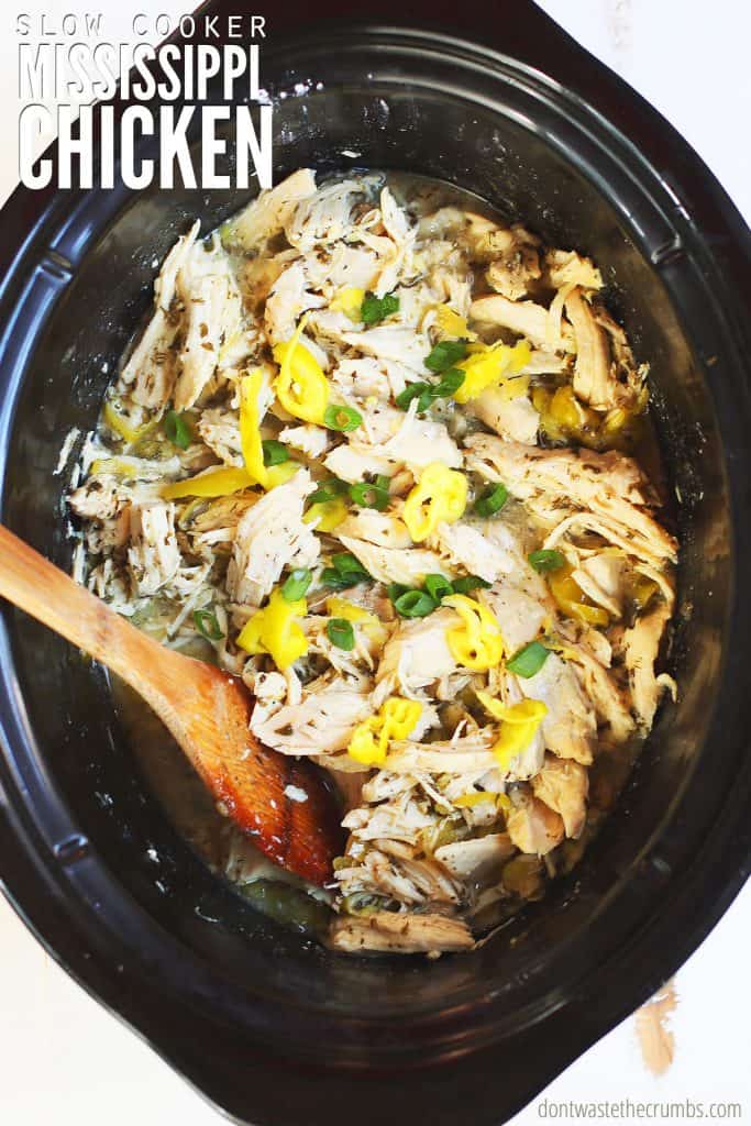 Crock Pot Mississippi Chicken recipe freshly cooked in a black oval slow cooker with chicken breast, cooked in broth, seasonings, pepperoncini, and finished with green onions. The text overlay reads 'Slow Cooker Mississippi Chicken.'