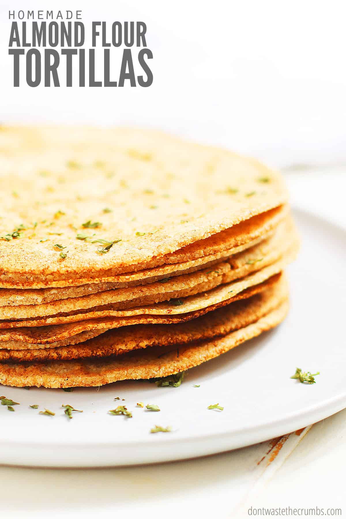 A stack of fresh homemade almond flour tortillas, sprinkled with a garnish of parsley. Text overlay reads "Homemade Almond Flour Tortillas."