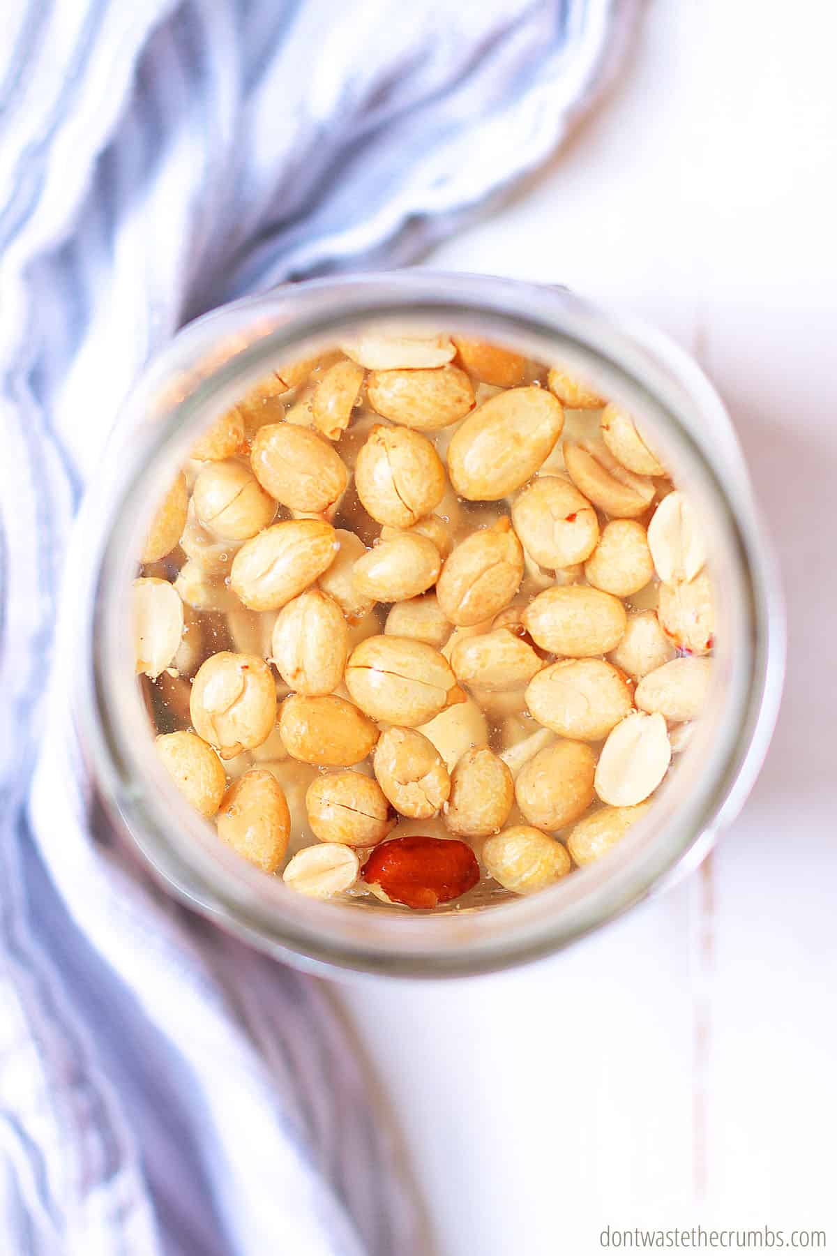 Whole peanuts soaking in a glass ball jar filled with water.