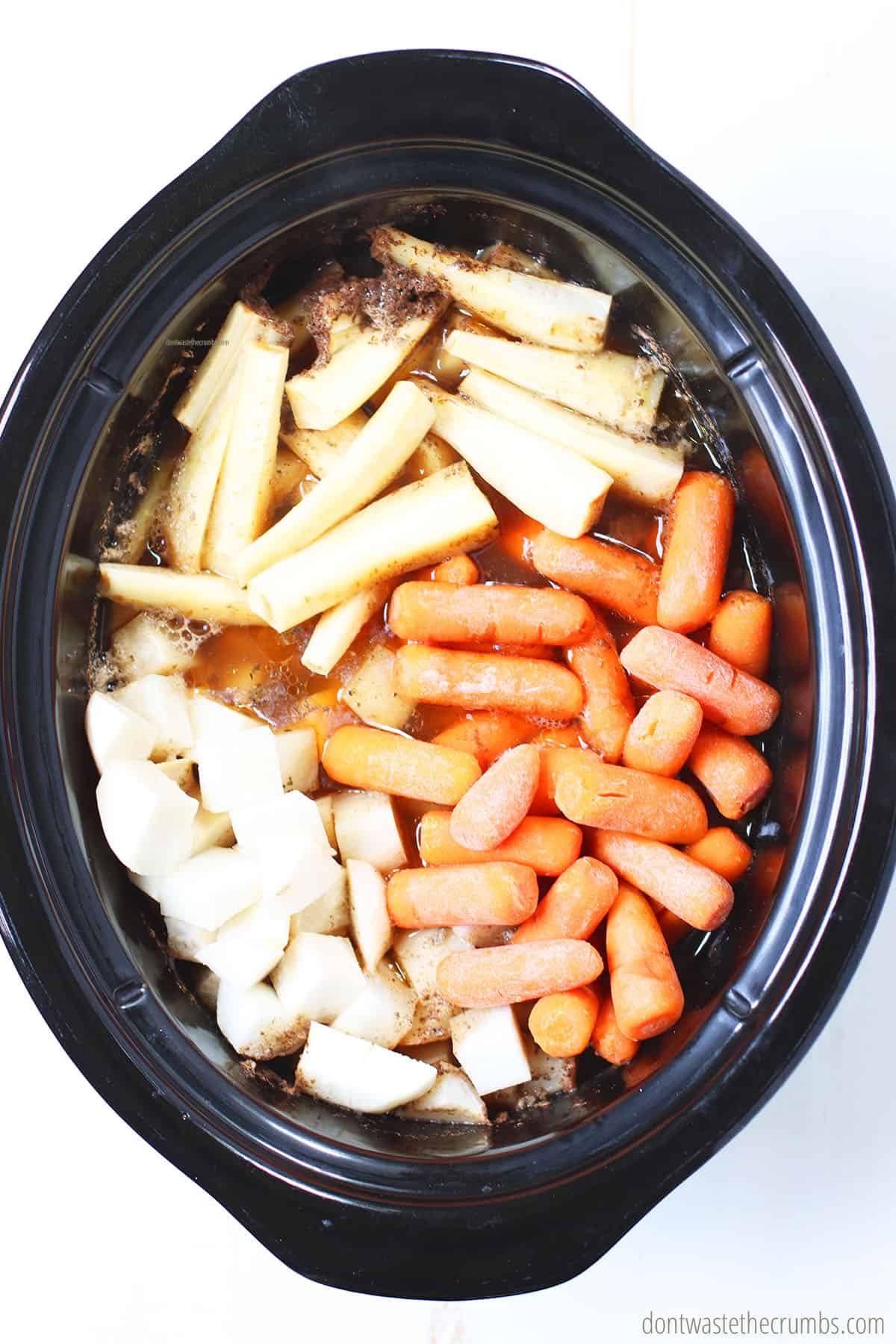 There is cut turnips, parsnips, carrots, and beef stock in the crock pot.