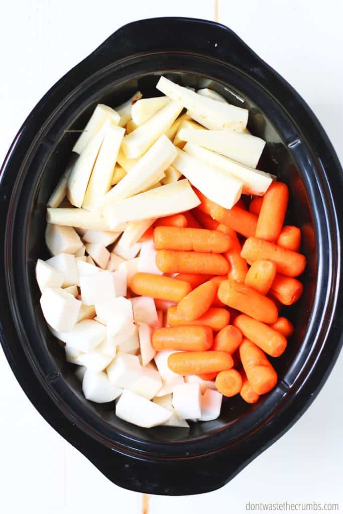 Fresh cut turnips, parsnips, and whole baby carrots are in the crock pot. These are some of the ingredients needed for this slow cooker beef stew.