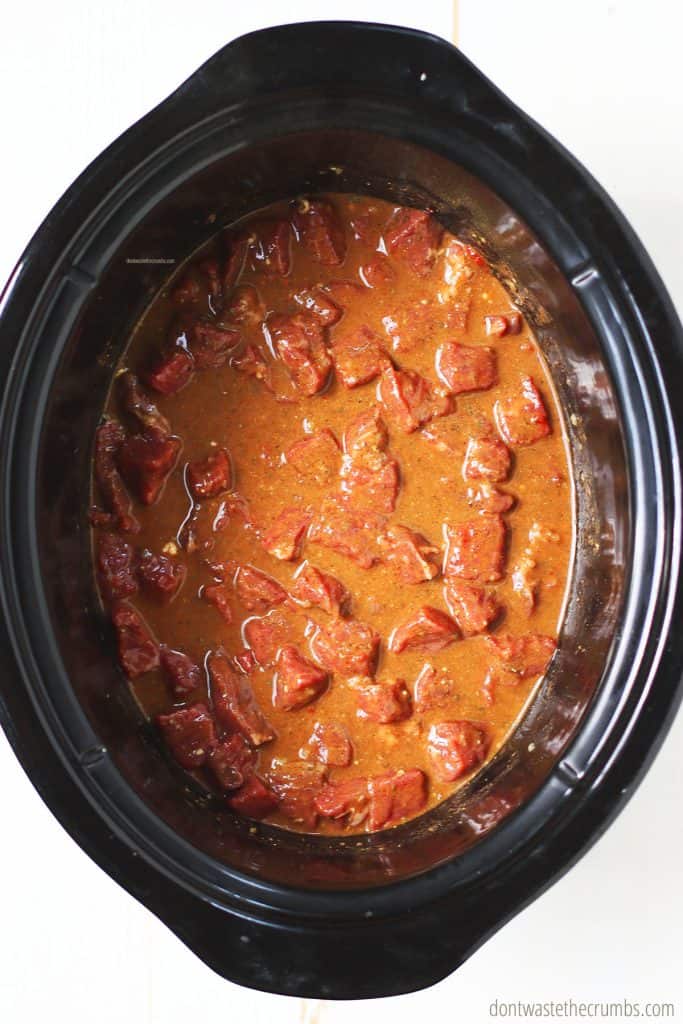 Chunks of meat, beef stock, and tomato paste are all mixed together in the crock pot.