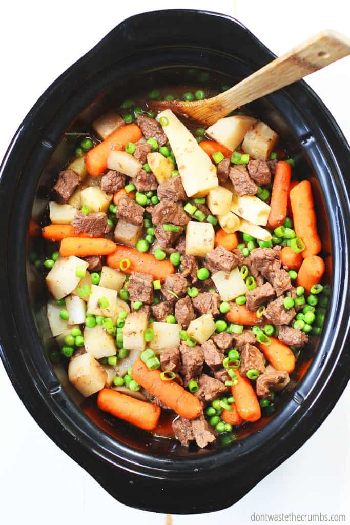 This slow cooker beef stew is ready! There is cut beef, parsnips, turnips, carrots, and peas in the crock pot.