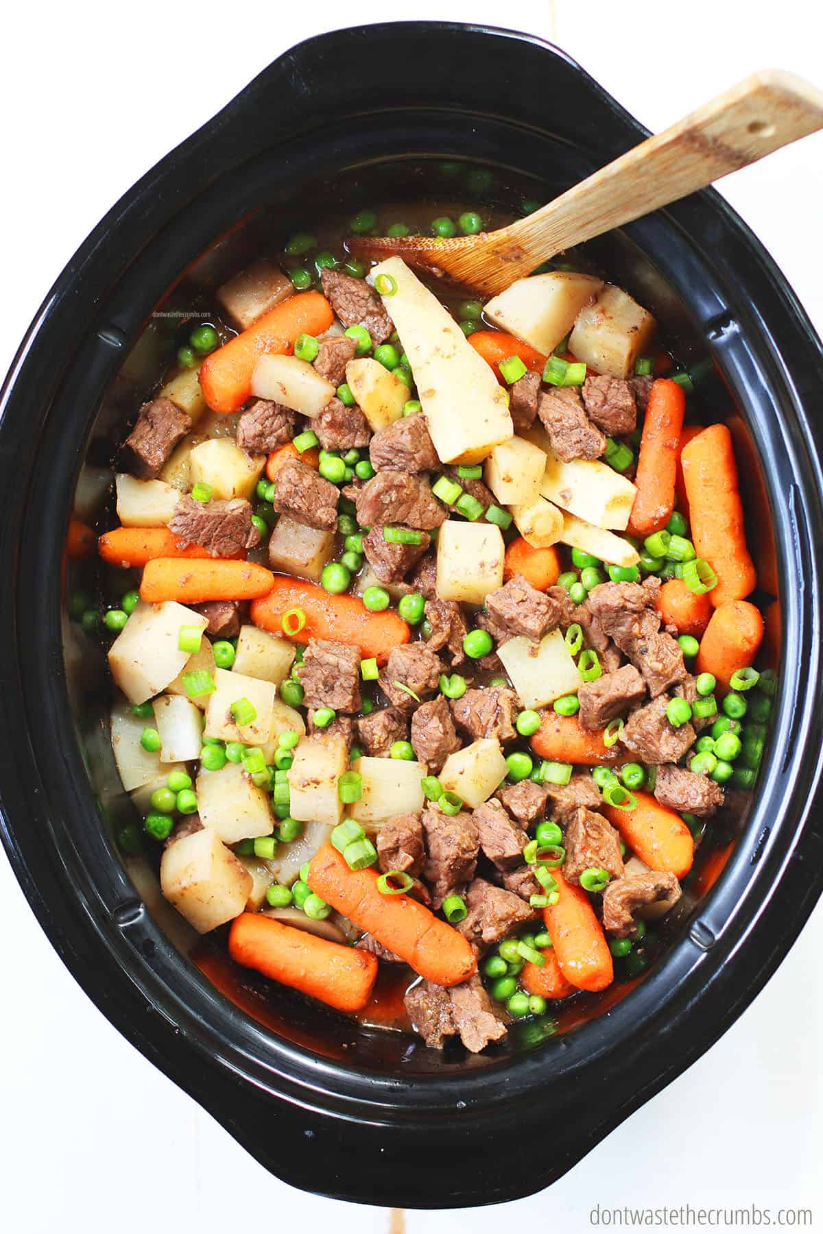 This slow cooker beef stew is ready! There is cut beef, parsnips, turnips, carrots, and peas in the crock pot.