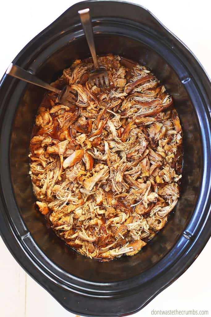 Two forks shred the cooked chicken shawarma thighs in the slow cooker
