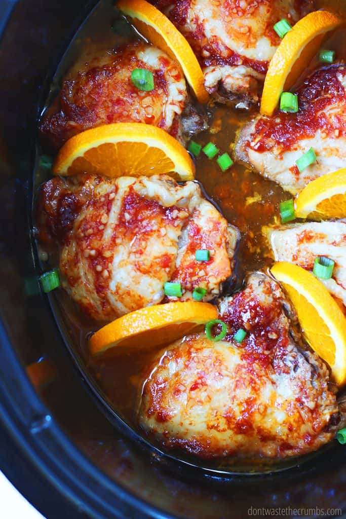 Perfectly roasted slow cooker chicken thighs ready to be served from the crockpot and garnished with orange wedges and sliced green onions