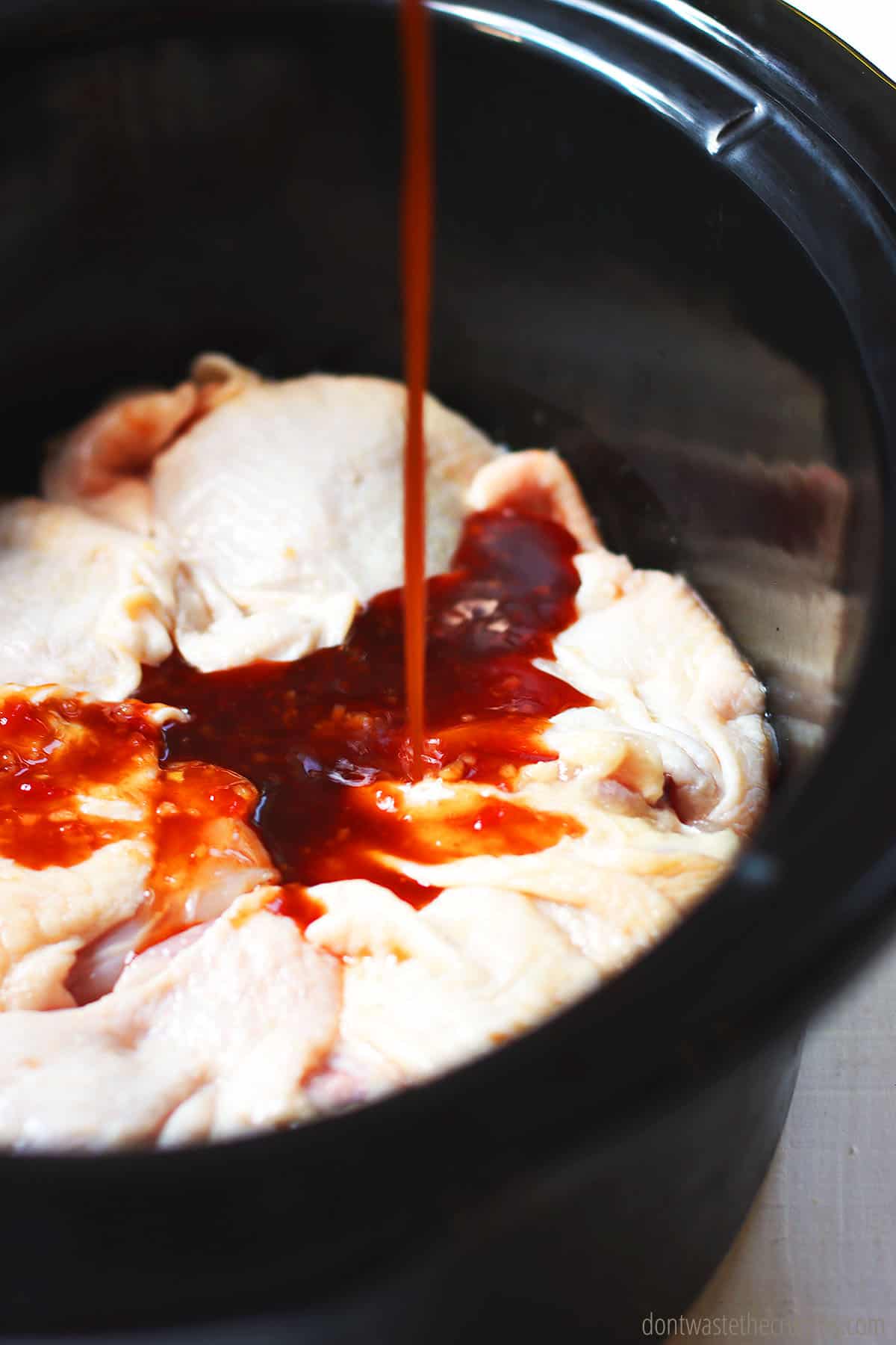 Sauce poured over raw chicken thighs in the crock pot, ready to be cooked as slow cooker chicken thighs