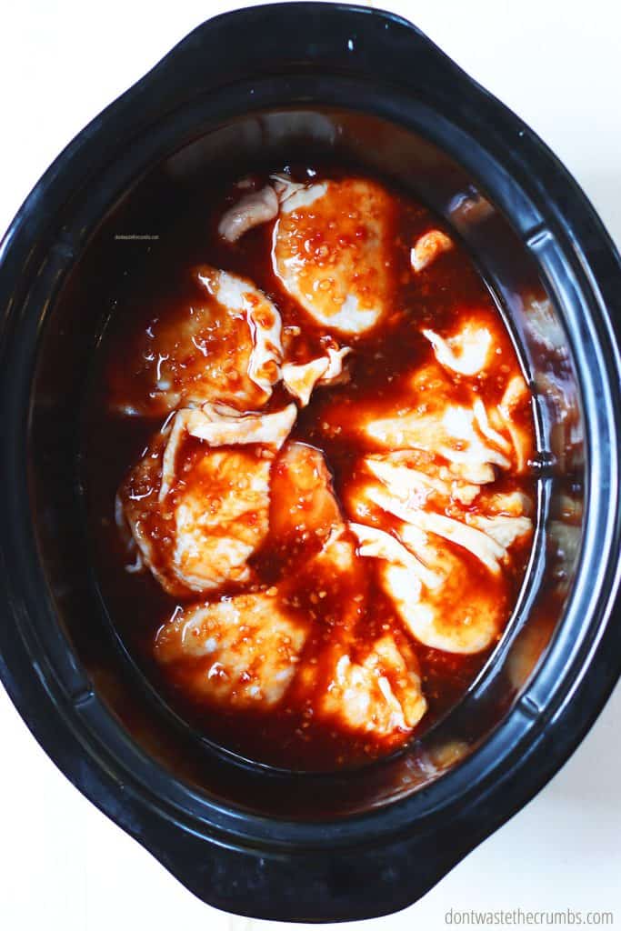 Raw slow cooker chicken thighs, covered in homemade sauce, ready to be cooked in the crockpot