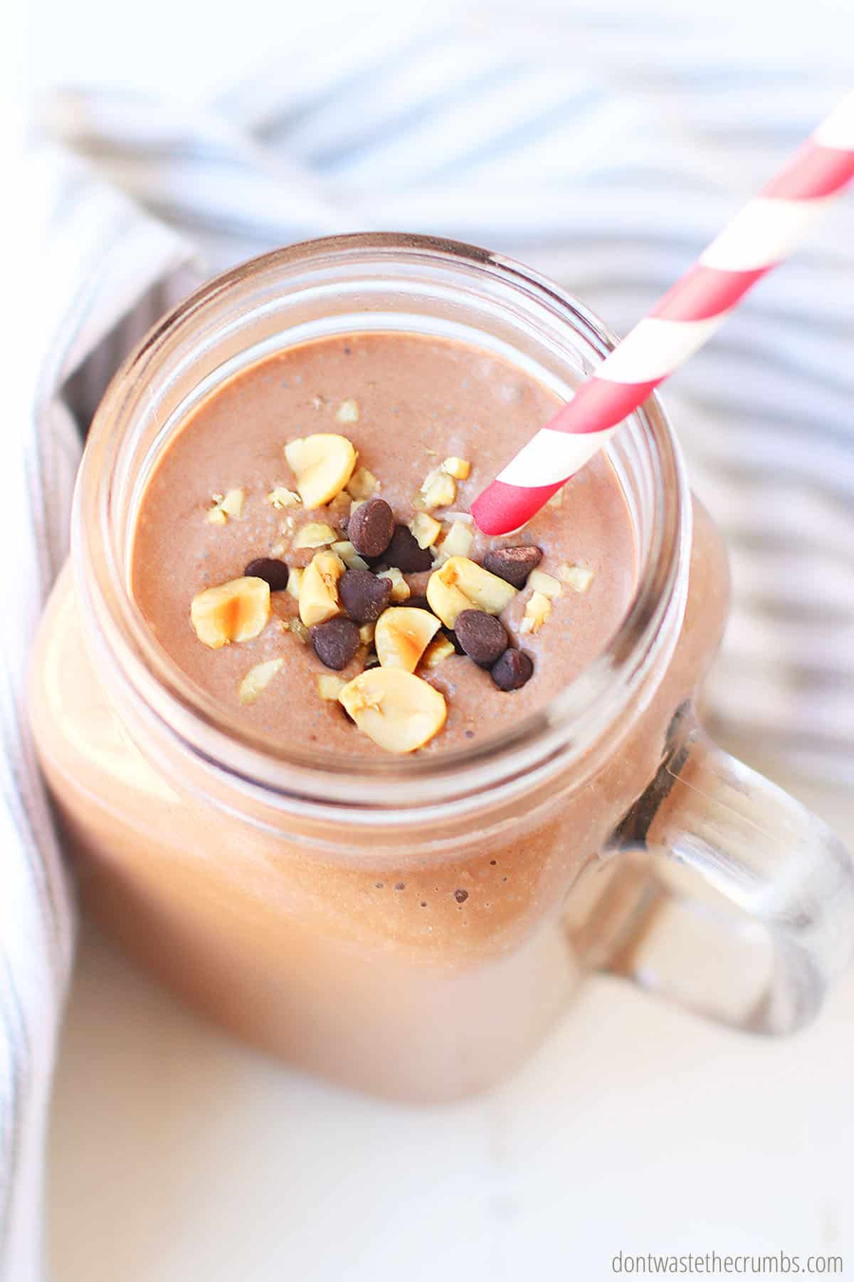 Looking down at the top of a chocolate peanut butter smoothie in a glass jar with a red and white striped straw. Garnished with chopped peanuts and chocolate chips.