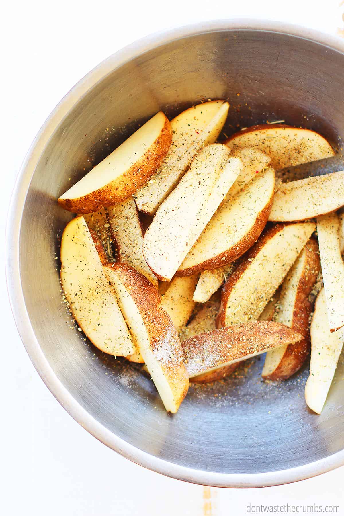 Sliced seasoned potato wedges in a large mixing bowl
