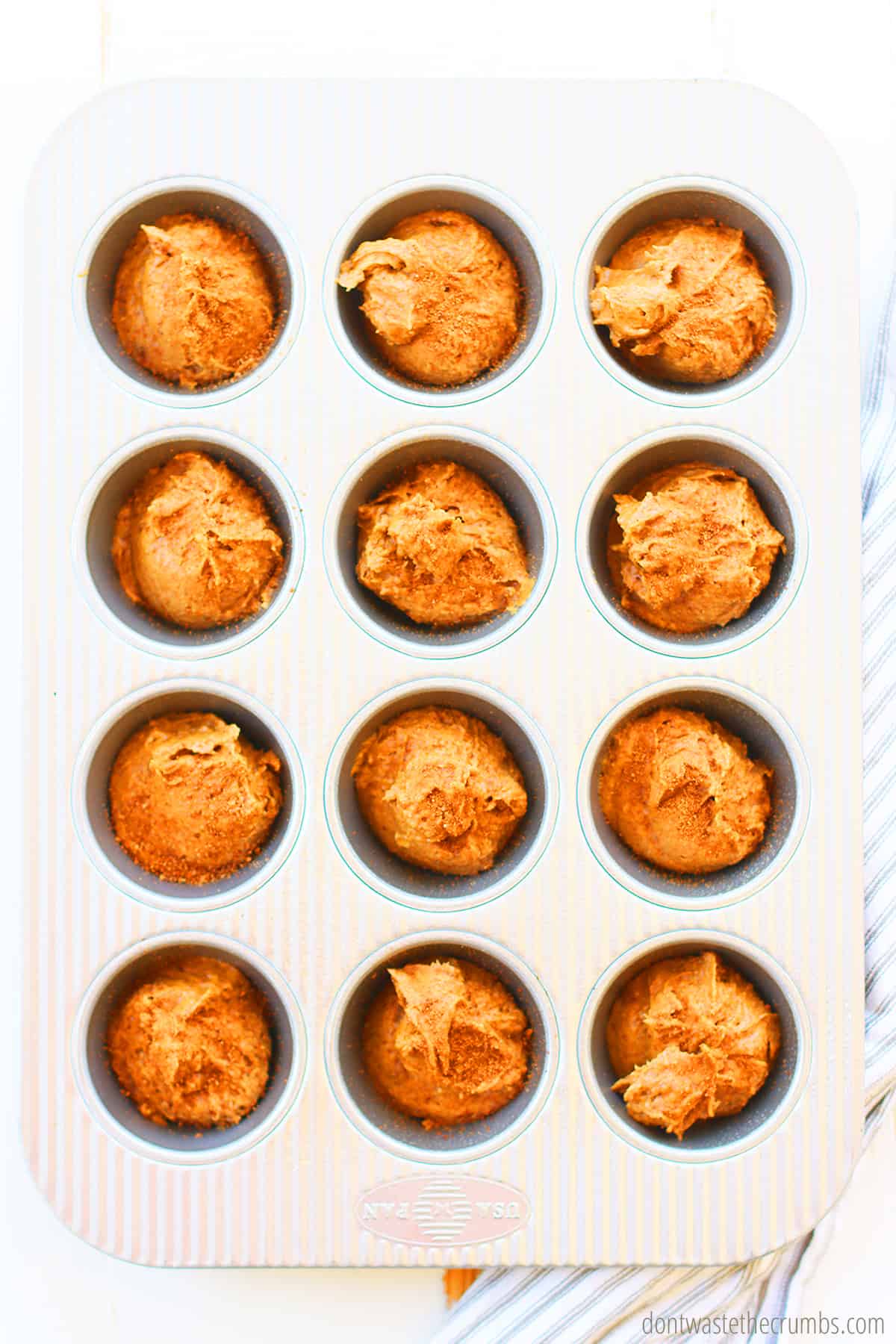 A prepared muffin tin with 1/4 cup mix measured into each muffin cup tin for this applesauce muffins recipe.