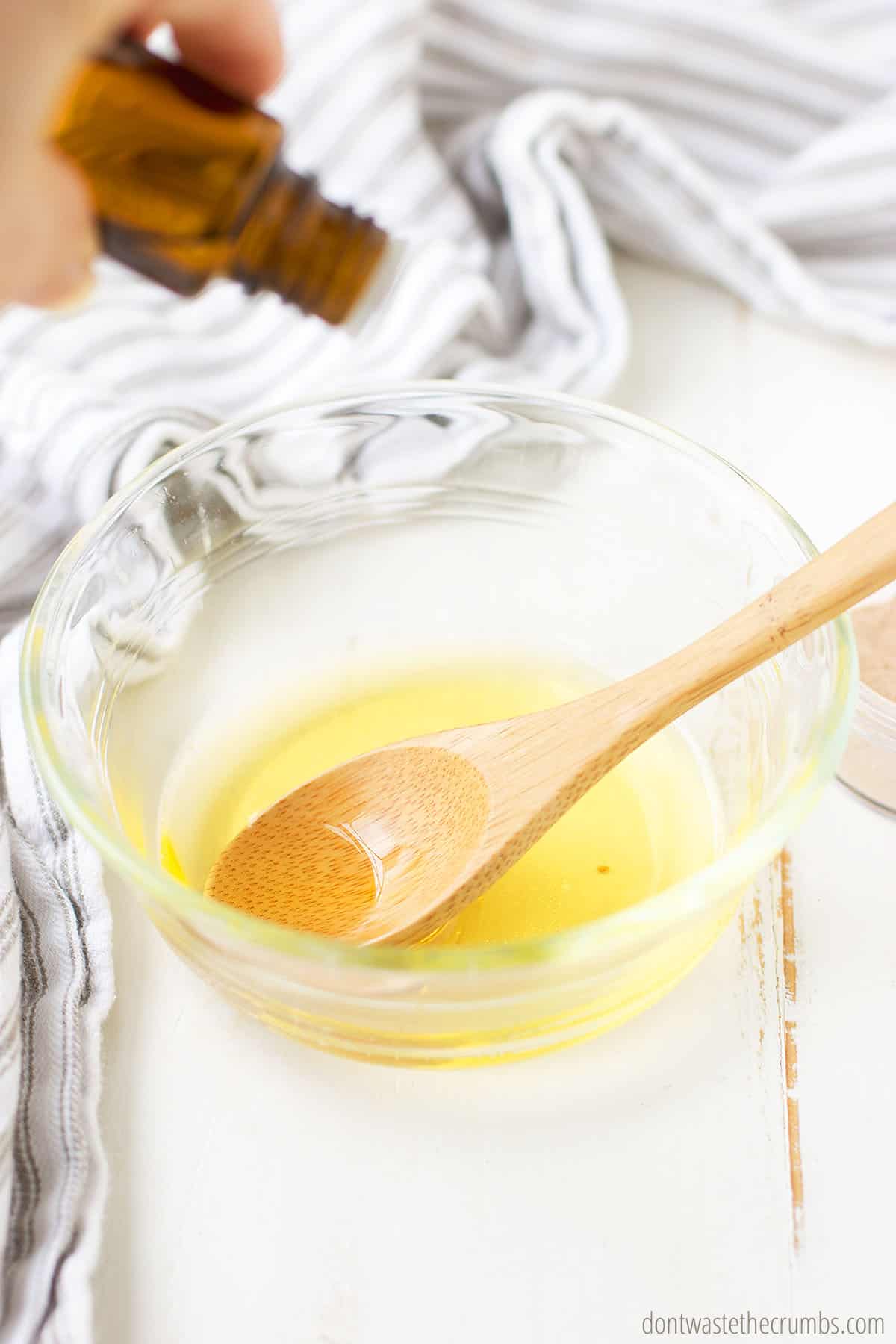 Oil and melted coconut oil in a glass bowl with a wooden spoon.