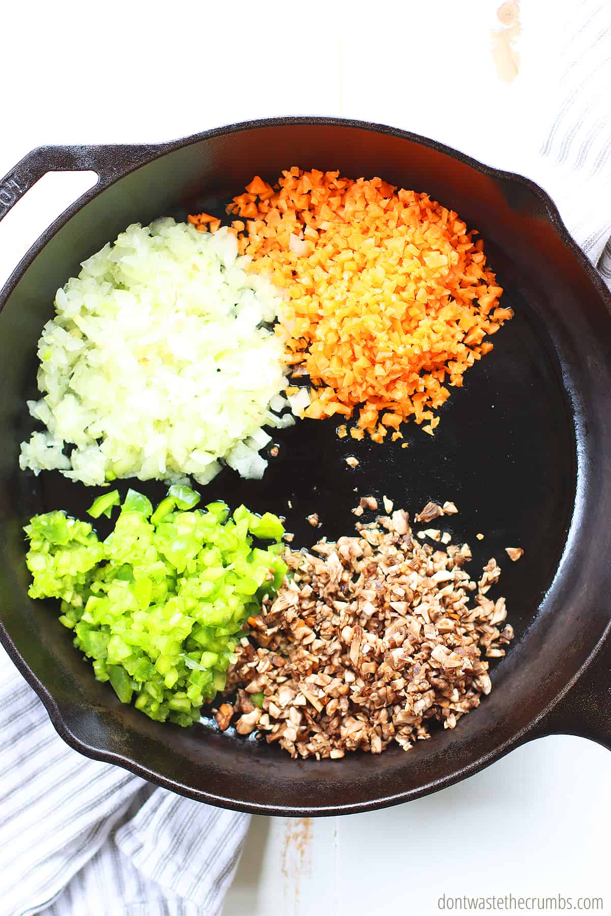 Chopped onion, carrot, mushrooms, and celery in their own sections in a cast iron skillet.