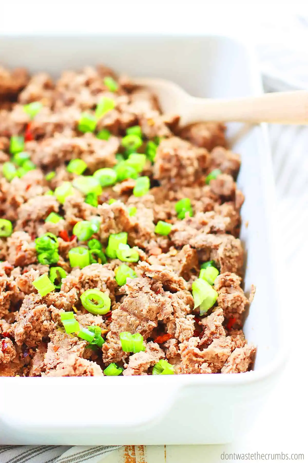 A white serving dish with freshly cooked ground beef from the Instant Pot. Garnished with chopped scallions and ready to be used in your favorite recipes. 