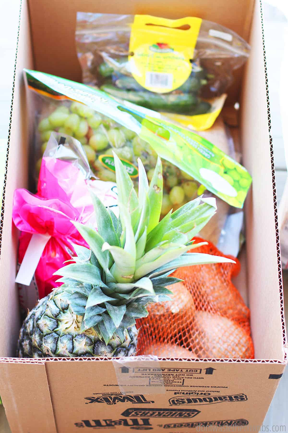 Cucumbers, grapes, sweet potatoes, pineapple and onion in a box that were ordered via the Instacart grocery delivery service.