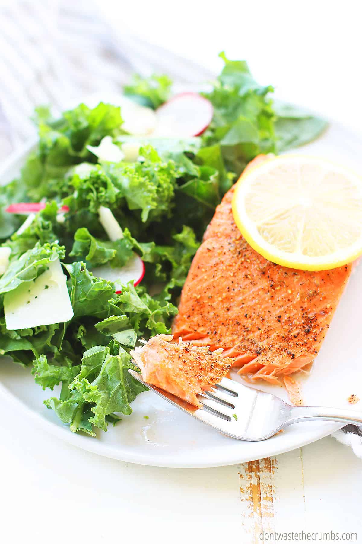 enjoy a forkful of lemon pepper salmon with a fresh salad and a lemon wedge. 